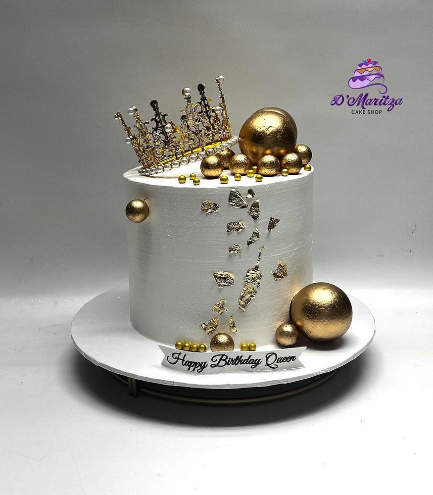 White cake topped with gold crown and spheres